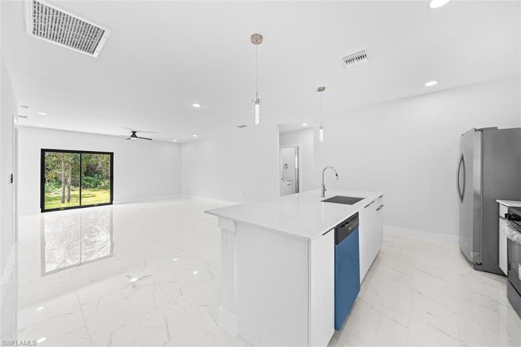 Bright white tile flooring, contemporary kitchen island with a white countertop and undermount sink, stainless steel appliances, modern ceiling fan, and sliding glass doors