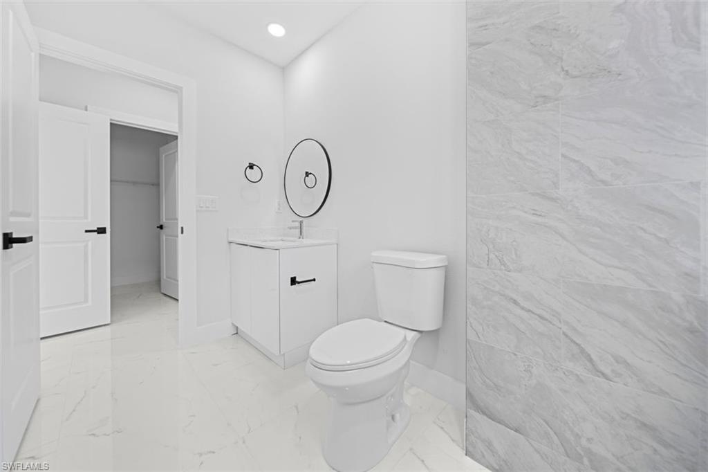 White vanity with integrated sink, black hardware, wall-mounted mirror, and tile flooring