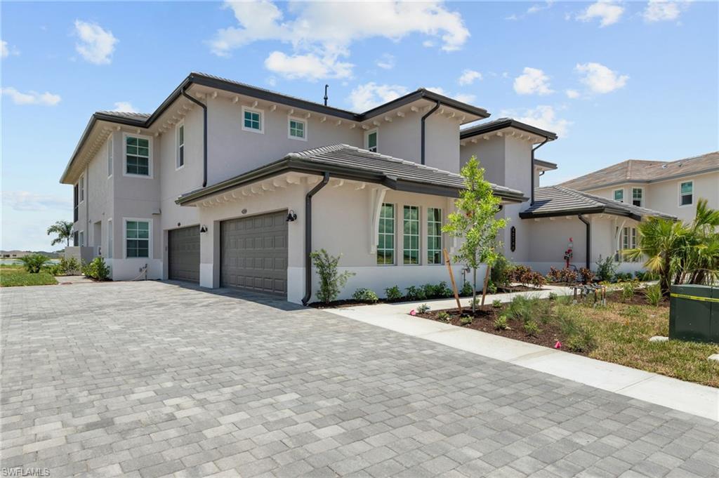 Stucco exterior with multiple windows, paver driveway, and an attached two-car garage