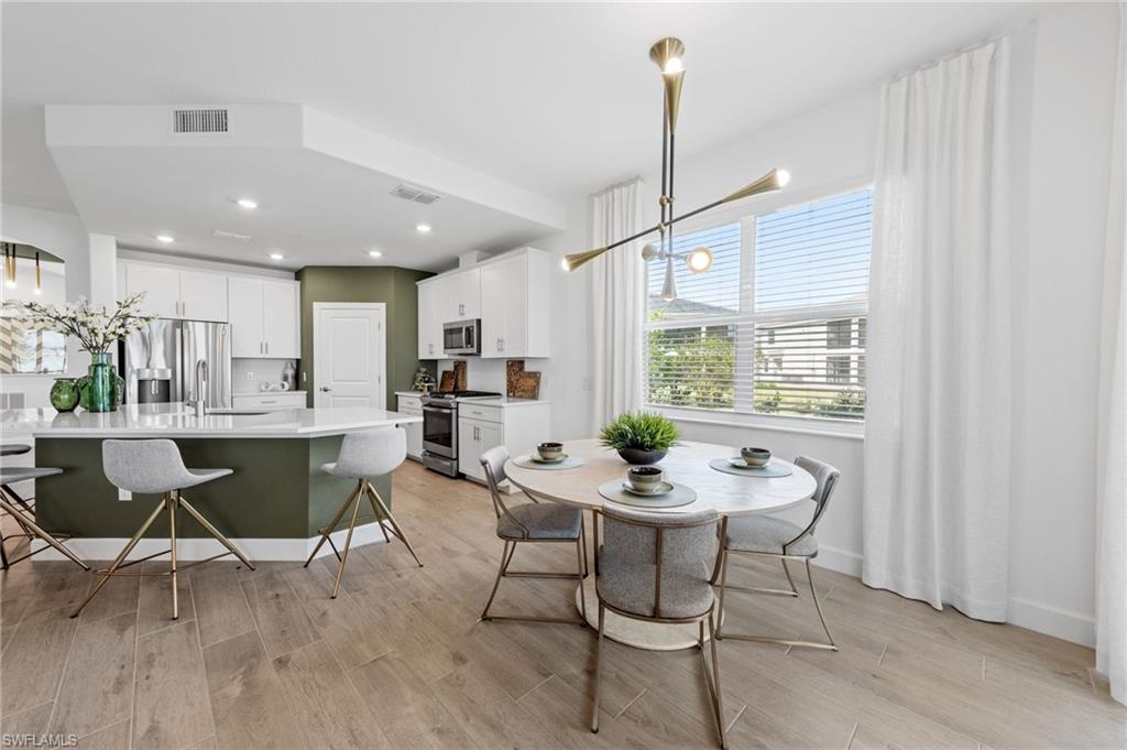 Open-concept space featuring wood-finish flooring, a kitchen island with stone countertop, white shaker-style cabinetry, and stainless steel appliances