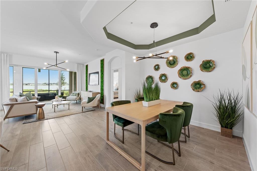 Expansive open-concept living area with wood-finish flooring, large sliding glass doors, and a decorative tray ceiling