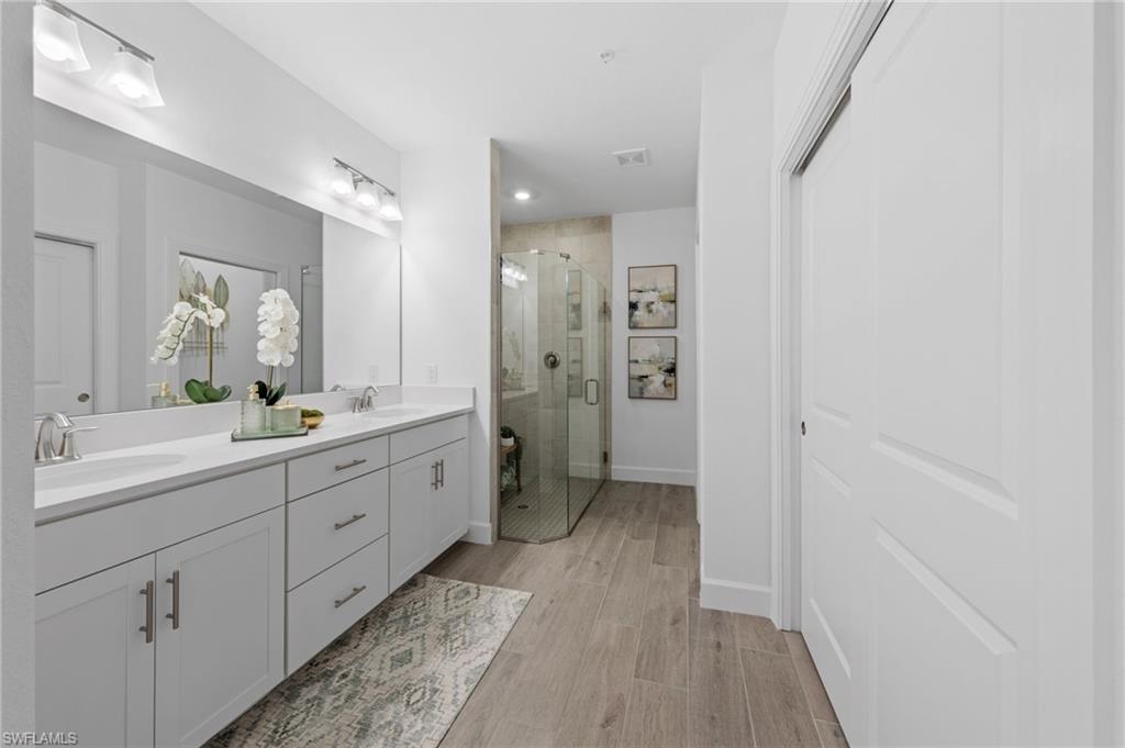 Dual vanity with integrated sinks, wood-finish flooring, a glass-enclosed shower, and a built-in closet with a panel door