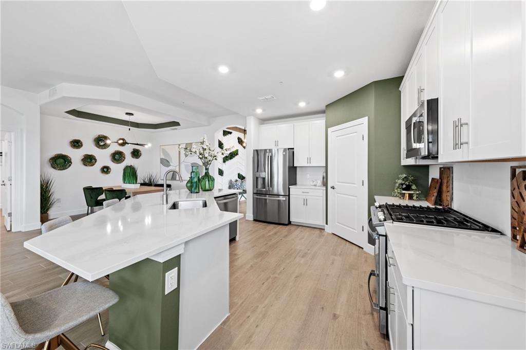 Expansive kitchen island with an undermount sink and faucet, white cabinetry, stainless steel appliances, and wood-finish flooring