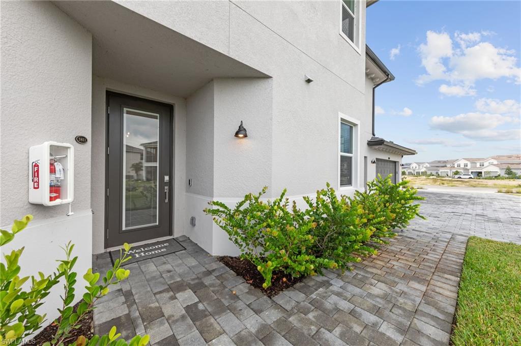 Stucco exterior with a glass-paneled entry door, a paver walkway, decorative outdoor lighting, and established shrubbery