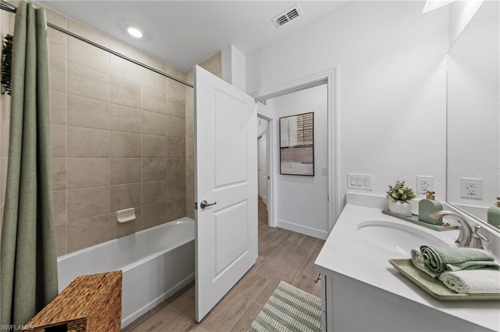 Full bathroom featuring a white tub with tile surround, wood-finish flooring, a single vanity with a white countertop, and an integrated sink