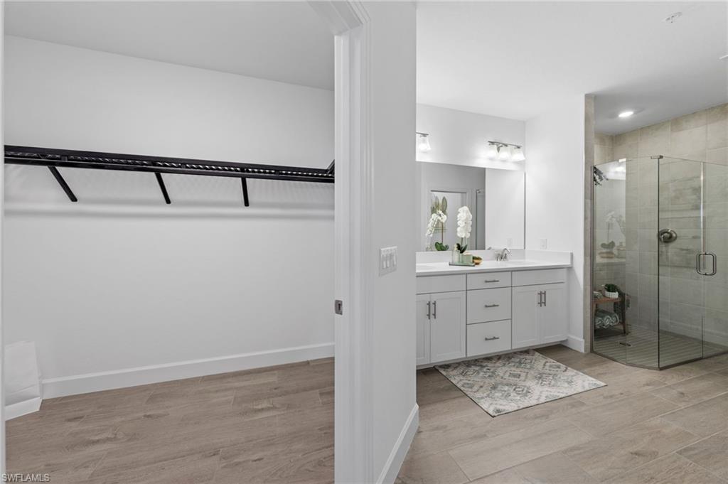 Wood-finish flooring throughout, dual vanity with a white countertop and undermount sinks, and a glass-enclosed shower with tiled walls