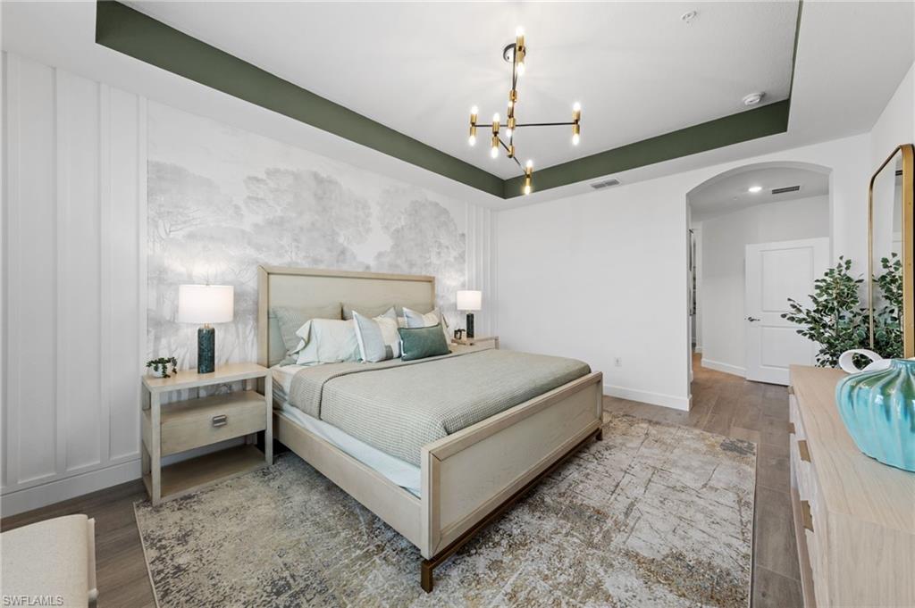 Tray ceiling with accent paint, modern chandelier, arched doorway, paneling detail, and wood-finish flooring