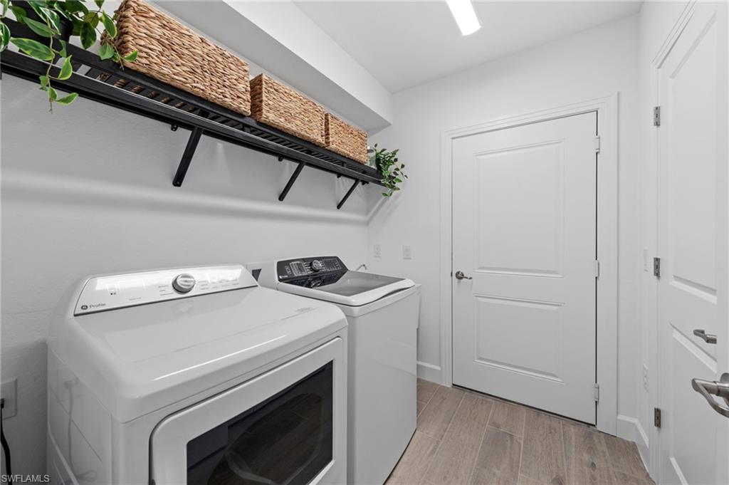 White laundry appliances with an overhead black metal shelving unit, wood-finish flooring, and white paneled doors