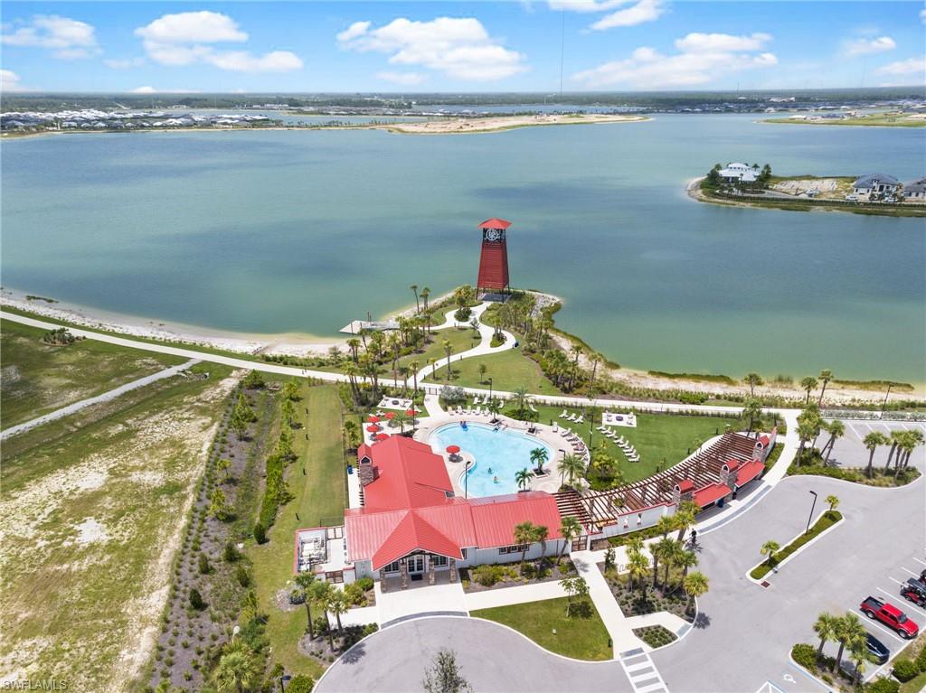 Community clubhouse with a swimming pool, waterfront access, a red lighthouse structure, and a paved parking area