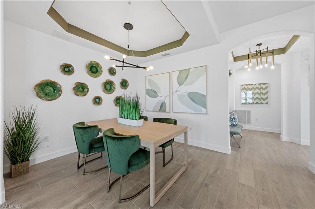 Tray ceiling with accent paint, modern chandelier, wood-finish flooring, and arched entryway
