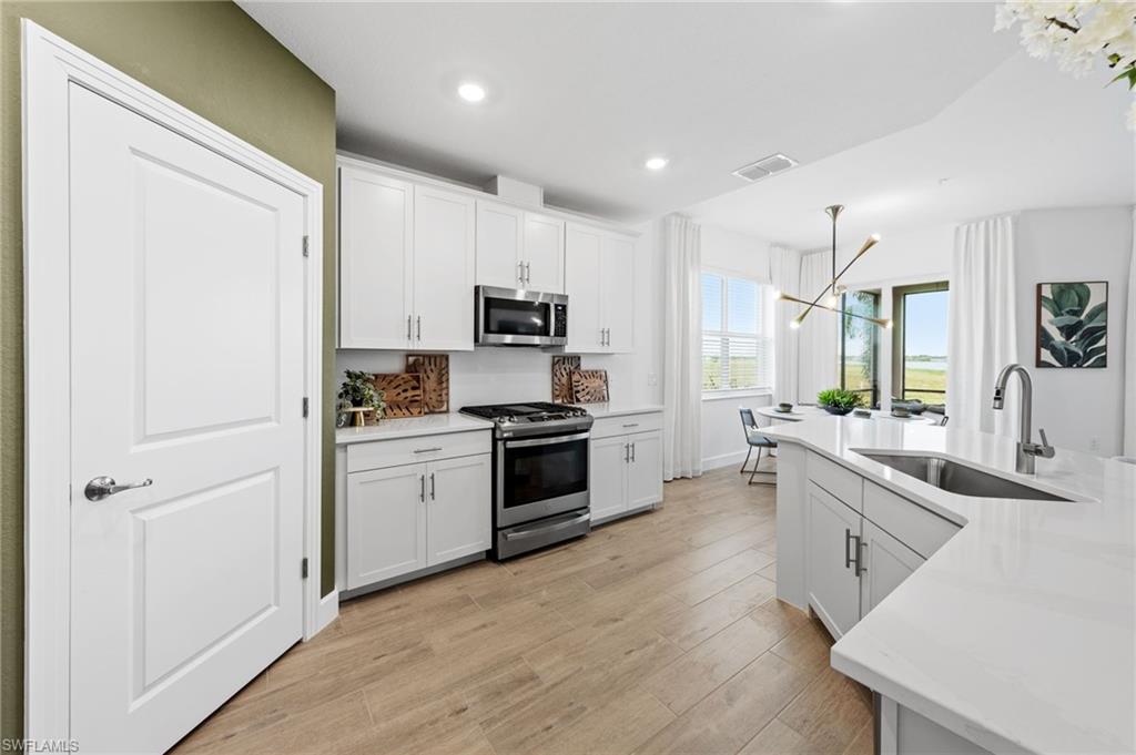 White cabinetry with stainless steel appliances, wood-finish flooring, and light-toned countertops