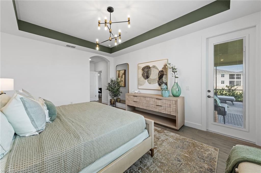 Tray ceiling with a decorative accent color, contemporary chandelier, and wood-finish flooring