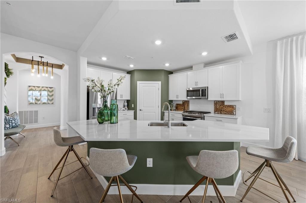 Kitchen featuring white cabinetry, stainless steel appliances, a large island with a sink, and wood-finish flooring