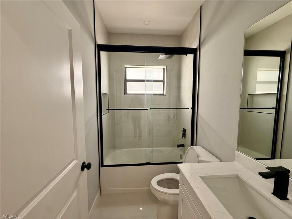 Sleek bathroom featuring a vanity with an integrated sink and quartz countertop, a matte black faucet, and a shower-tub combination with a glass enclosure and black trim