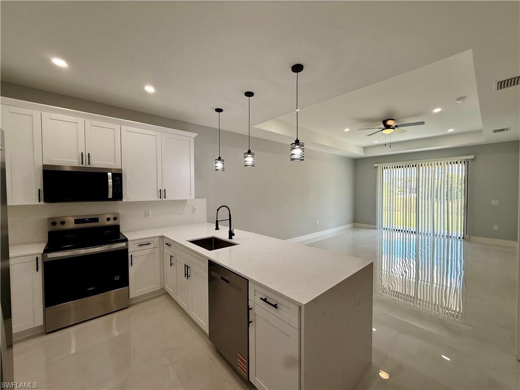 Open-concept kitchen featuring white cabinetry, stainless steel appliances, and a central island with a sink