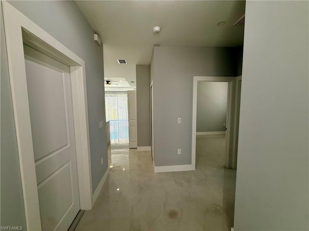 Recessed lighting illuminating a hallway with light-toned tile flooring, light gray walls, and white trim