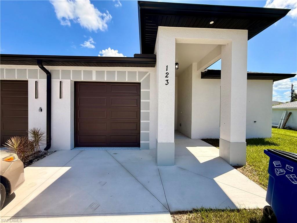Contemporary stucco exterior with a dark shingle roof, two distinct covered entryways, dark wood-finish garage doors, and a concrete driveway