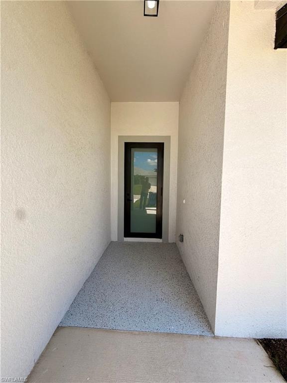 Recessed entryway with textured stucco walls, a modern black-framed door with a full-lite design, and a speckled gray hard-surface landing