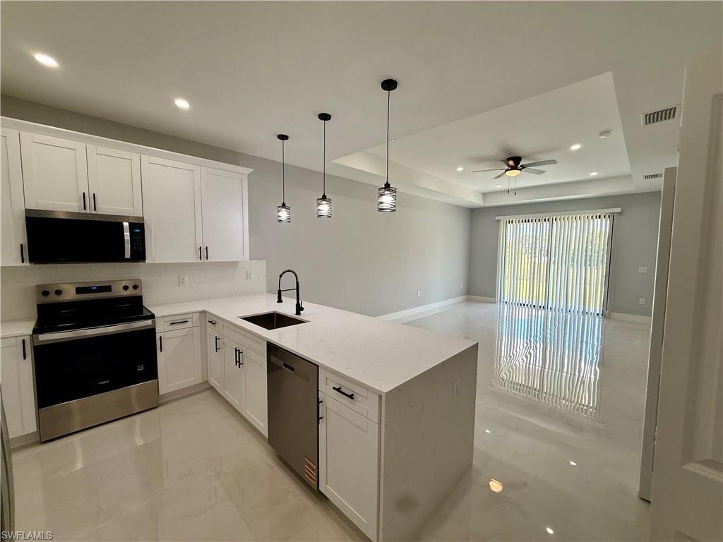 Kitchen featuring white cabinetry, stainless steel appliances, a white countertop island with an undermount sink, and pendant lighting