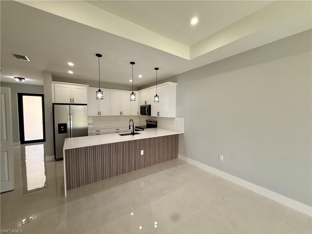 Contemporary kitchen featuring white cabinetry, stainless steel appliances, a breakfast bar with textured wood-finish paneling, and recessed lighting