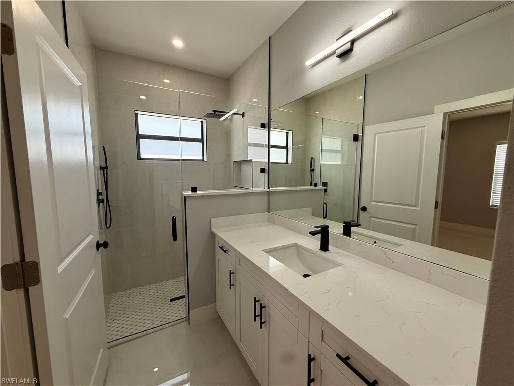 Spacious bathroom featuring a double vanity with stone countertops, a large mirror, and a glass-enclosed shower with a rainfall showerhead