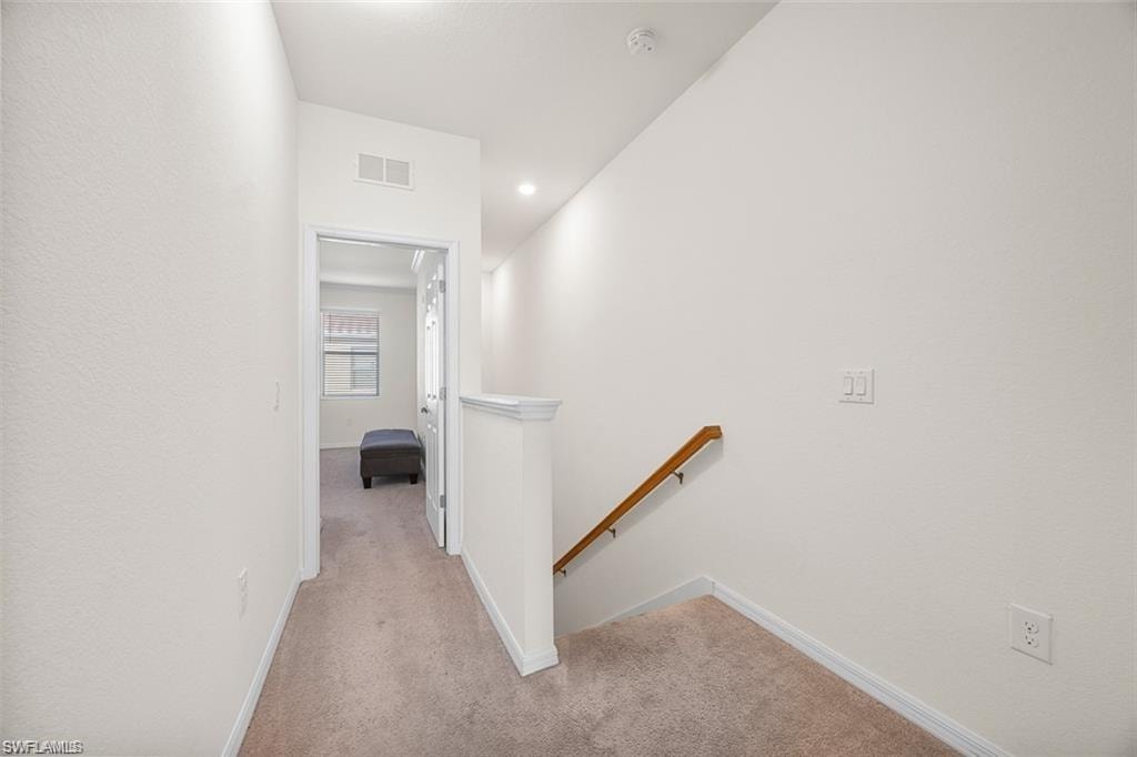 Carpeted hallway with a wood handrail, white balustrade, and recessed lighting