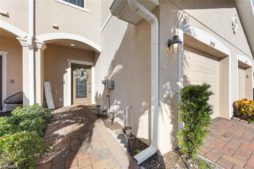 Stucco exterior with an arched entryway, paver walkway, attached garage, and exterior lighting fixture