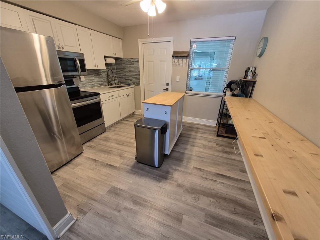 Left unit Kitchen featuring stainless steel appliances, white cabinetry, tile backsplash, wood-finish flooring, and a ceiling fan