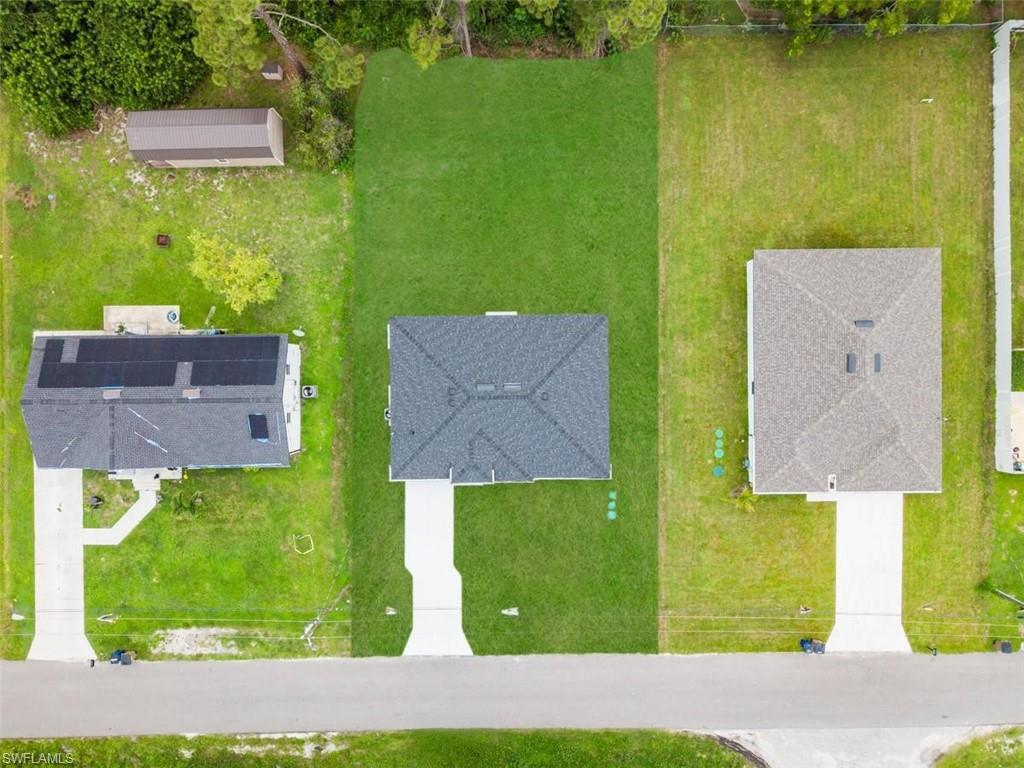 Expansive lot featuring a green lawn, concrete driveway, and a partially developed surrounding area