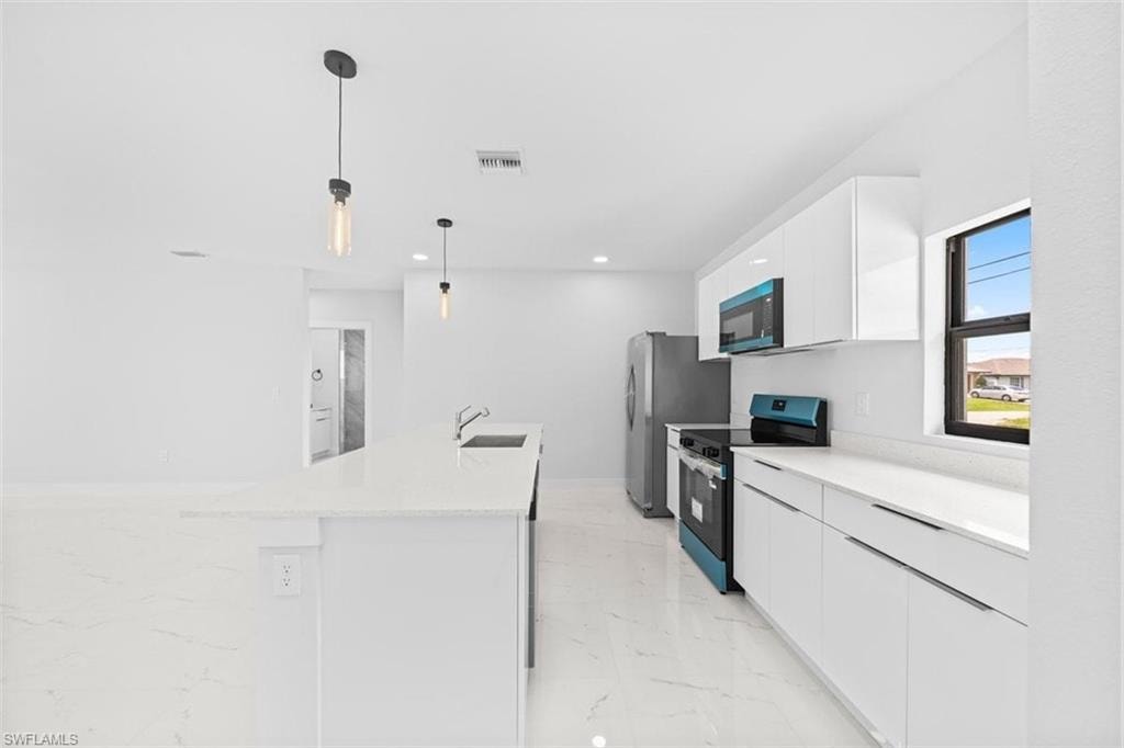 Kitchen featuring a large central island, white cabinetry, integrated sink, and stainless steel appliances