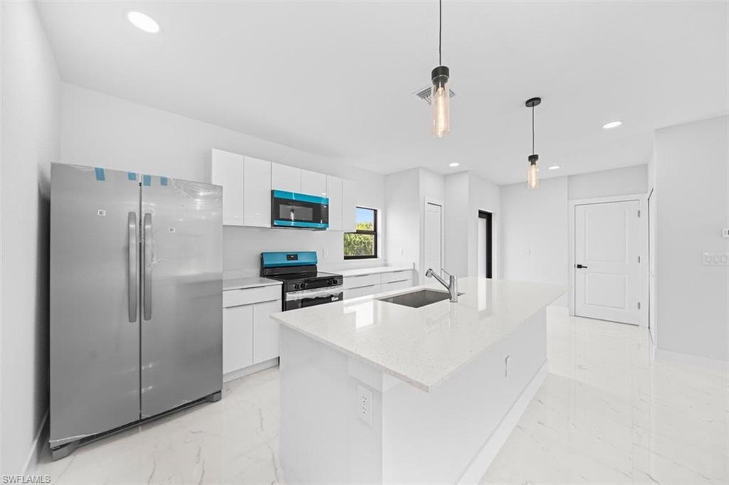 White shaker cabinetry with modern hardware, stainless steel appliances, central island with an undermount sink, recessed lighting, and pendant lighting