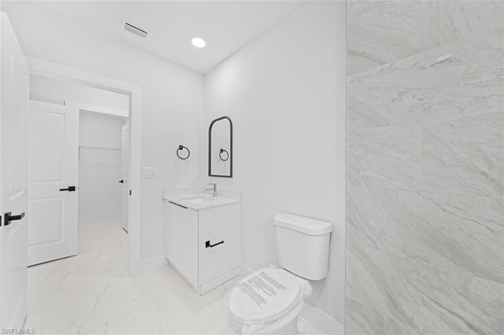 White vanity with a single basin sink, wall-mounted mirror, and contemporary black fixtures