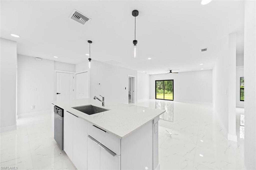 Open-concept living area featuring a kitchen island with sink, white shaker cabinetry, stainless steel appliances, and large format tile flooring