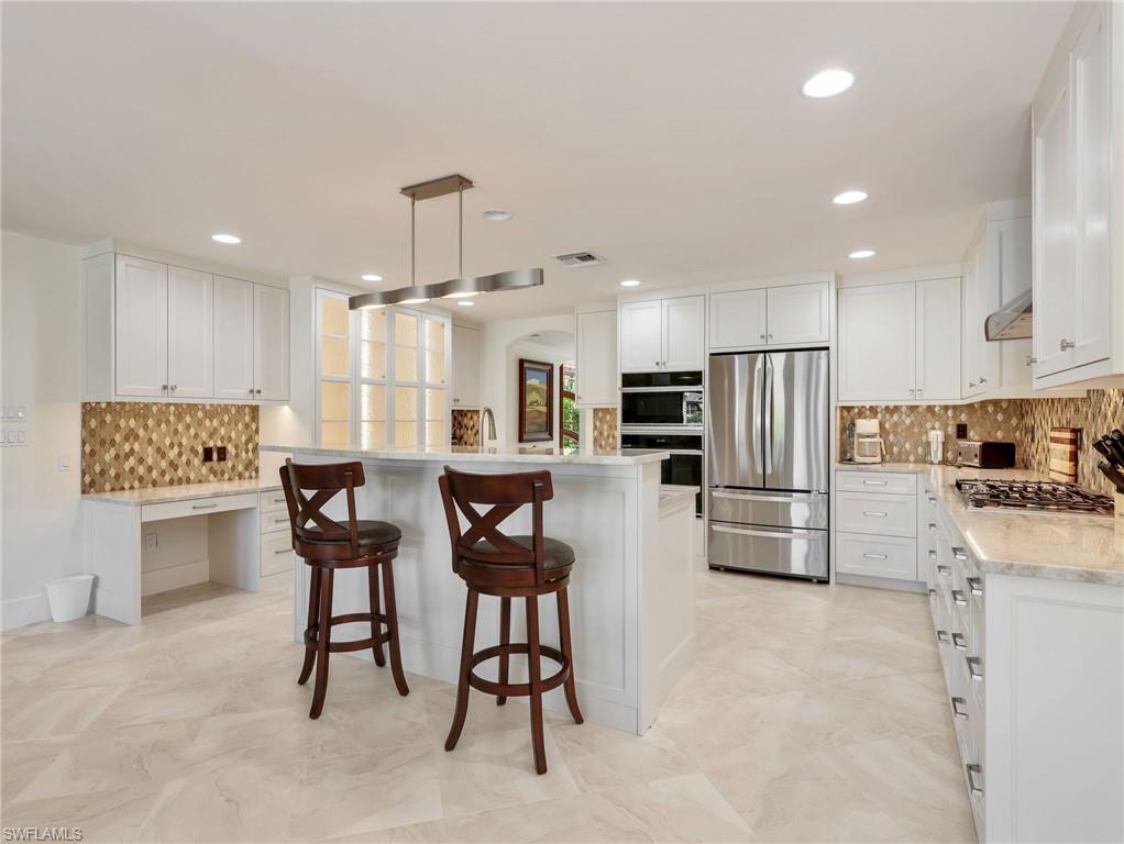 White cabinetry with brushed nickel hardware, stainless steel appliances, patterned backsplash, light-toned tile flooring, and recessed lighting