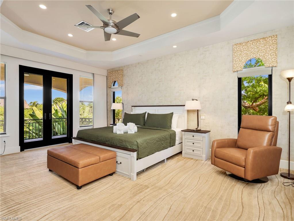 Tray ceiling with recessed lighting and ceiling fan, direct access to an outdoor balcony, white wood-frame bed with built-in storage, textured wall finishes, and wood-finish flooring