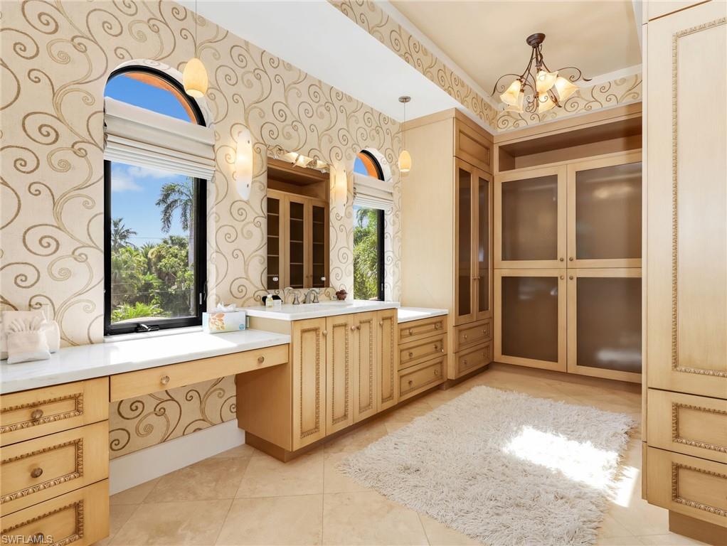 Stone tile flooring, custom built-in cabinetry, arched windows, built-in vanity, and decorative wallpaper