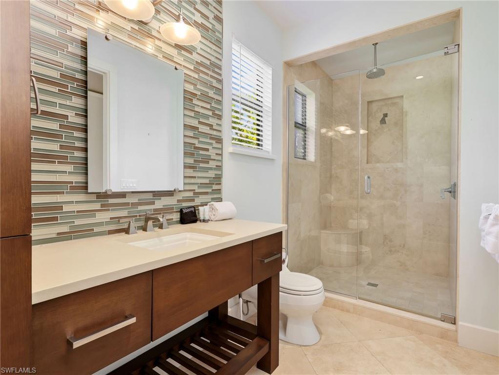 Vanity with integrated sink and chrome fixtures, mosaic tile backsplash, frameless glass shower enclosure, built-in shower niche, and ceiling-mounted showerhead