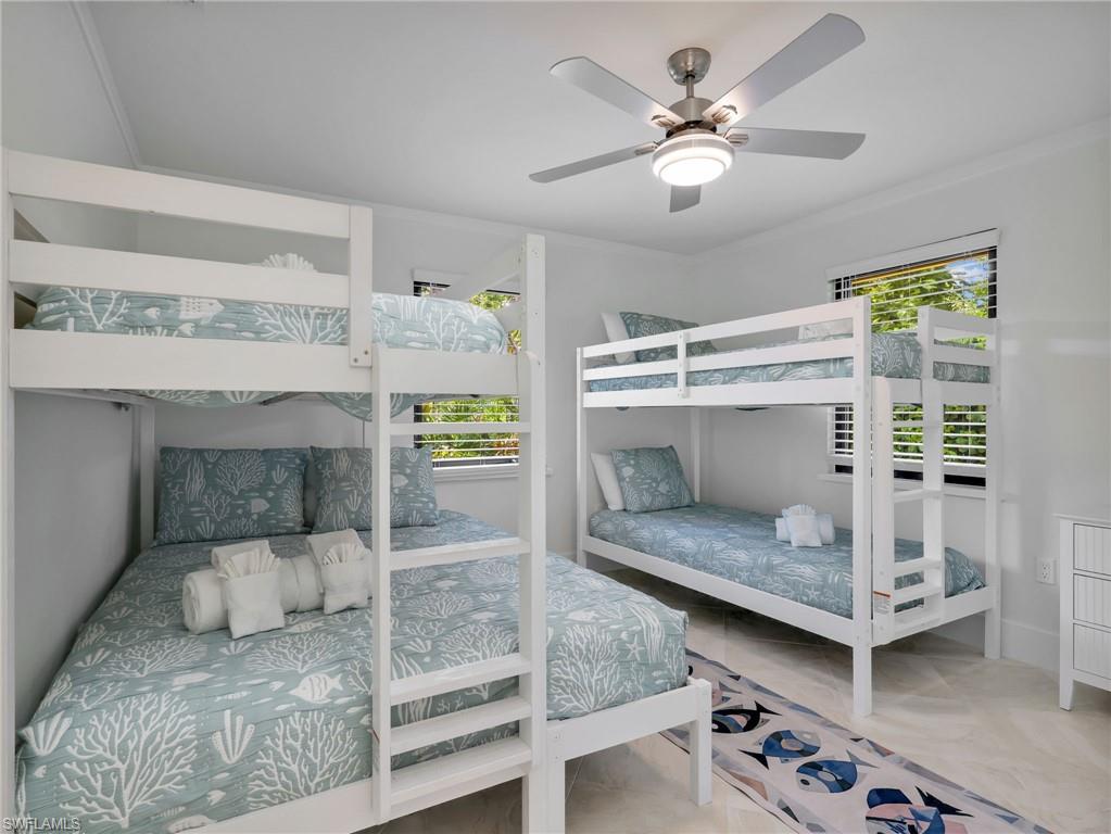 Bright room featuring two white bunk beds, a ceiling fan with integrated lighting, and multiple windows with horizontal blinds