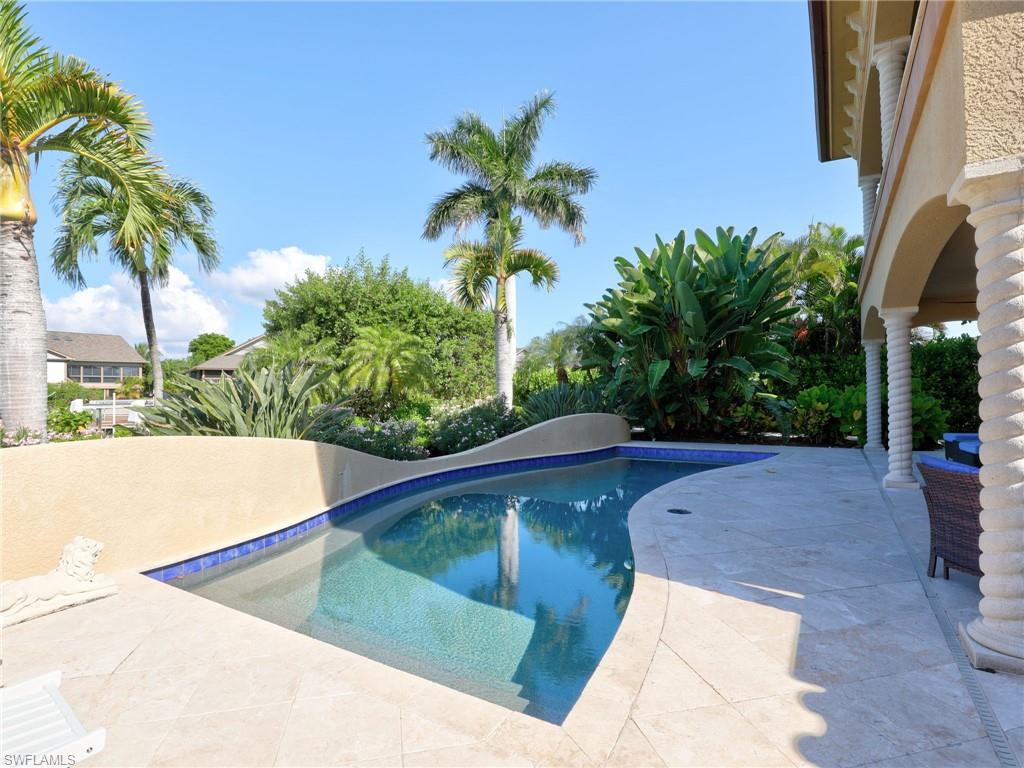 Resort-style backyard oasis featuring a sparkling saltwater pool with sun shelf, surrounded by expansive travertine decking