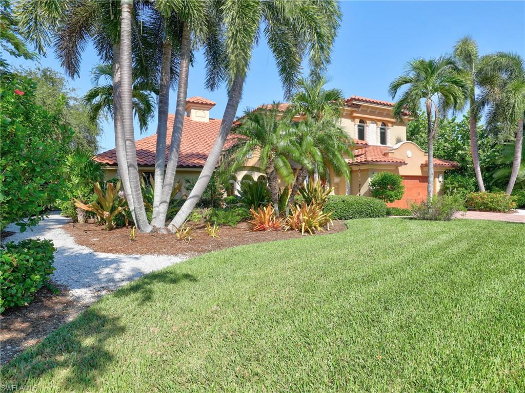 Tropical-inspired landscaping frames this Mediterranean-style residence, featuring mature palm trees, lush greenery, and a manicured lawn
