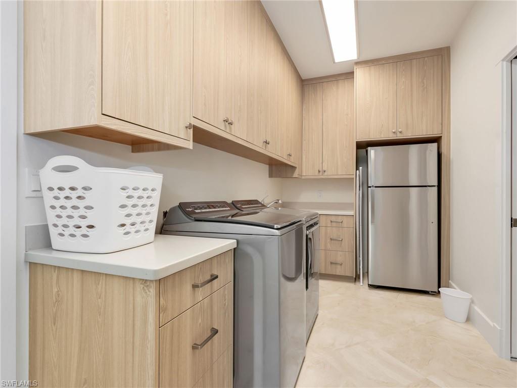 Full-height cabinetry with wood-finish, light-toned tile flooring, and integrated stainless steel refrigerator