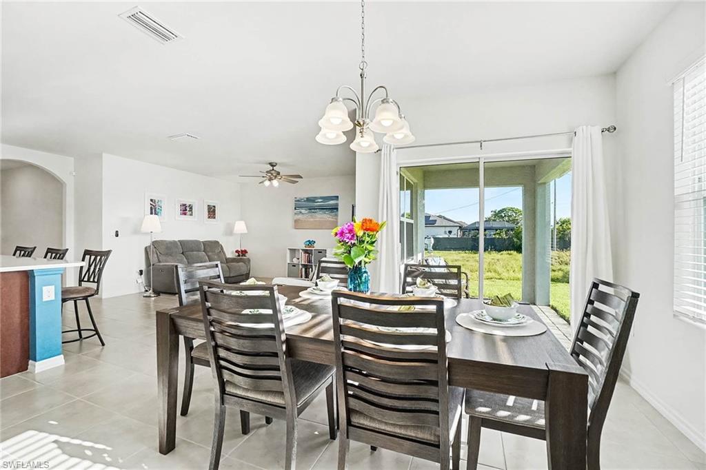 Open-concept living area featuring light-toned tile flooring, a dining space with a chandelier, and sliding glass doors leading to an outdoor area
