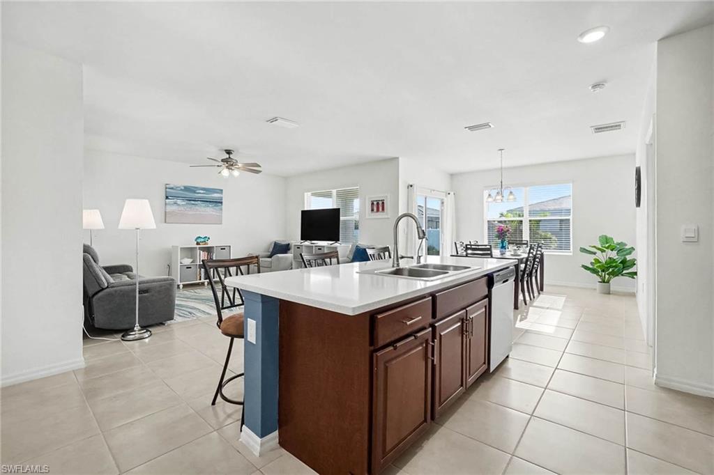 Open-concept living space featuring an island kitchen with a stainless steel sink, a dining area with a contemporary chandelier, and a living area with a ceiling fan