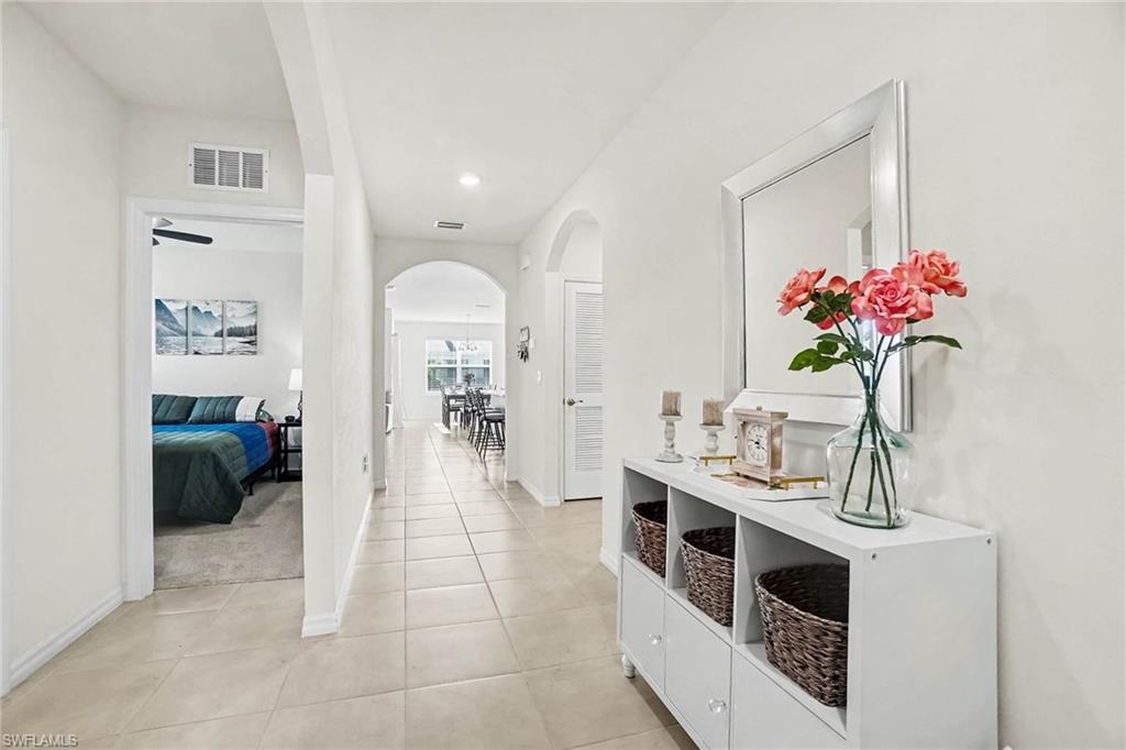 Tiled flooring throughout the hallway, arched entryway, recessed lighting, and a white interior color palette