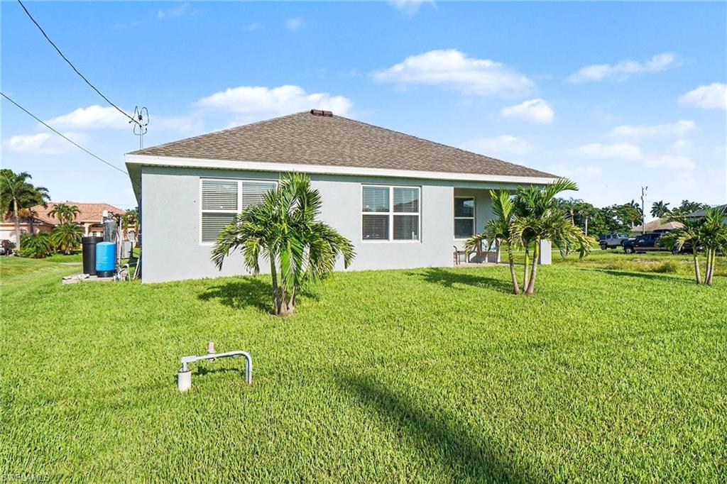 Expansive green lawn with established palm trees, light-colored exterior, and a covered patio area
