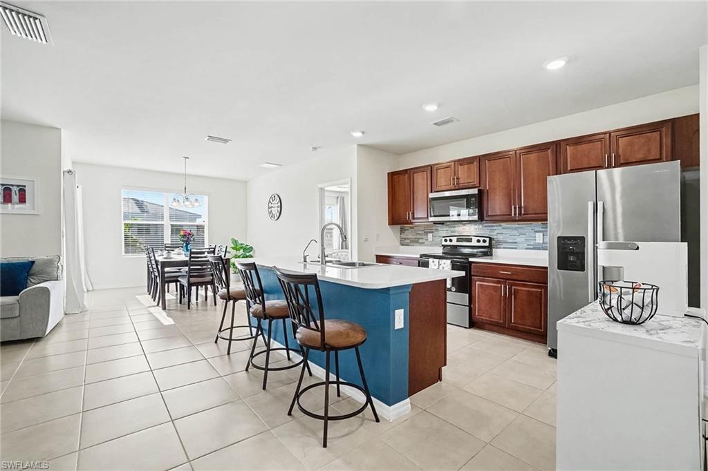 Open-concept living space with tile flooring, a kitchen island featuring a breakfast bar, wood cabinetry, stainless steel appliances, and a tiled backsplash