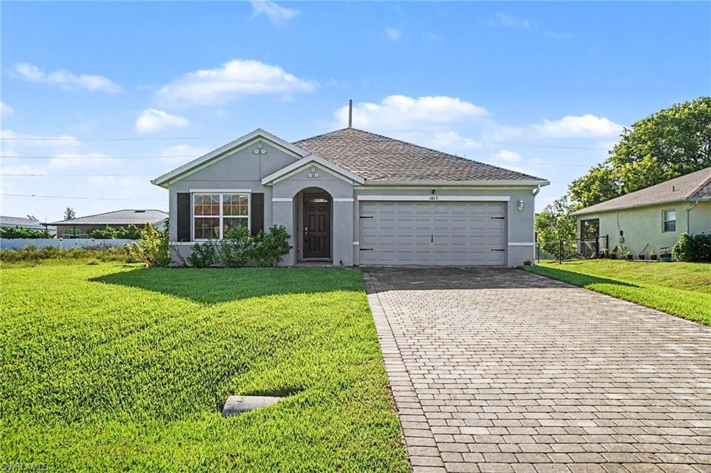 Single-story residence featuring a paved driveway, attached garage, arched entry, and shuttered window accents