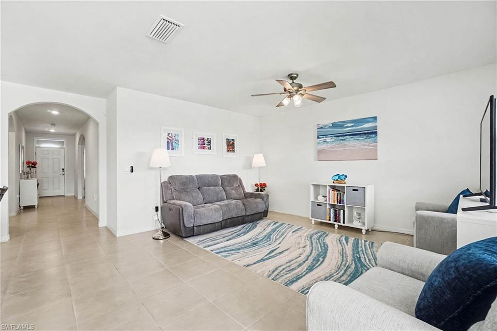 Spacious living area featuring large format tile flooring, a ceiling fan with integrated lighting, and an arched entryway