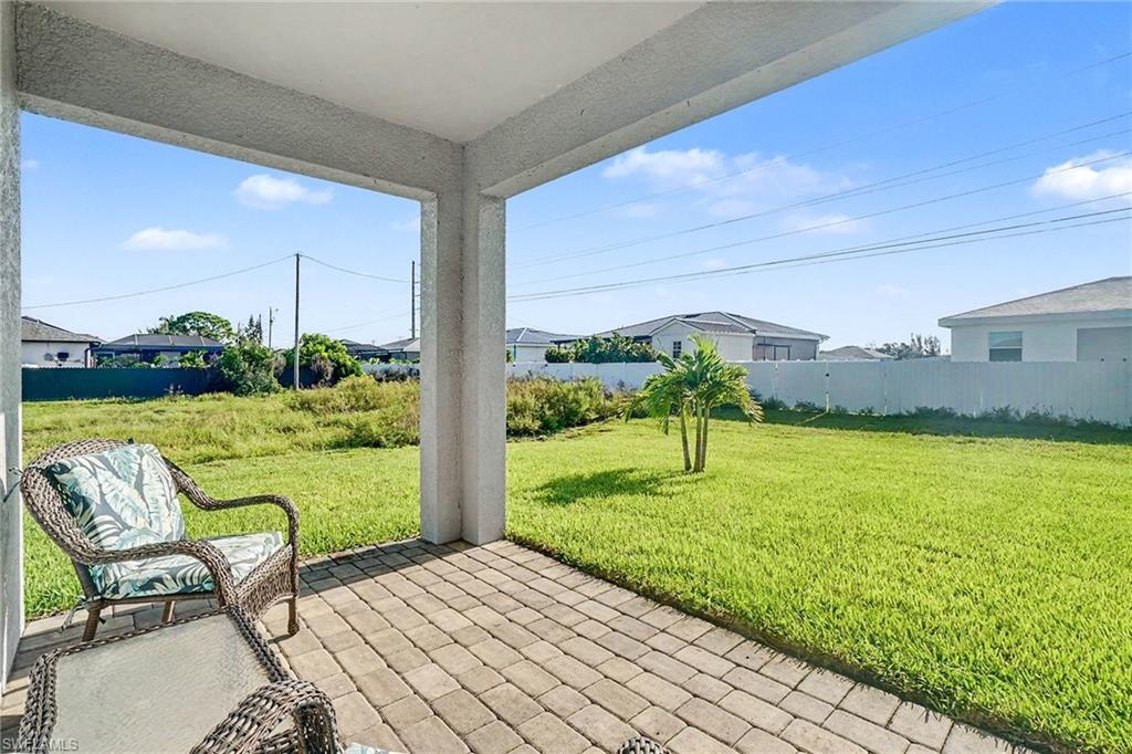 Covered patio with paver flooring, expansive grass lawn, and white privacy fencing