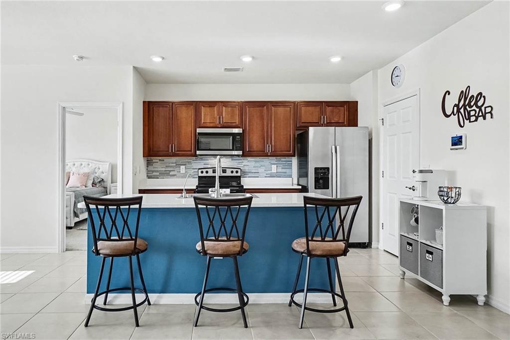 Kitchen featuring a blue-toned island with seating, stainless steel appliances, wood cabinetry, and tiled flooring